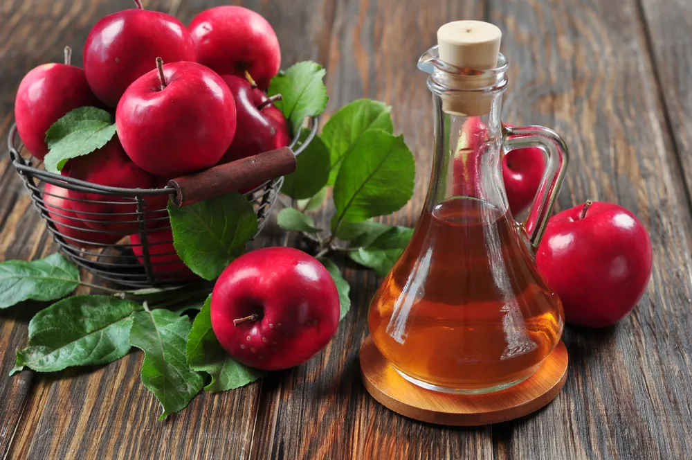 A bowl of apples beside a flask of apple cider vinegar