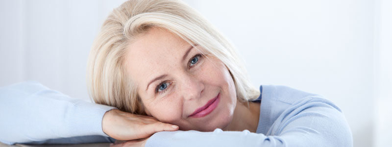 Femme mûre souriante reposant sa tête sur ses bras - Bannière de l'article Comment savoir si je suis ménopausée ? - ShytoBuy France