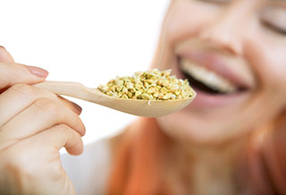 Femme souriante s'apprétant à manger une cuillère de graines de fenugrec pour augmenter sa poitrine - Fenugrec : l'ingrédient idéal pour une poitrine plus grosse