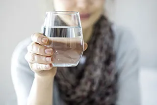 Femme tenant un verre d'eau eu premier plan - Comment soulager les symptômes de la ménopause ? - ShytoBuy France