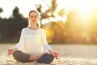 Femme assise en tailleur en train de méditer sur une plage de sable fin - Ménopause : comment soulager les symptômes de la ménopause ? - ShytoBuy France